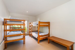 A room with three bunk beds and a bench.