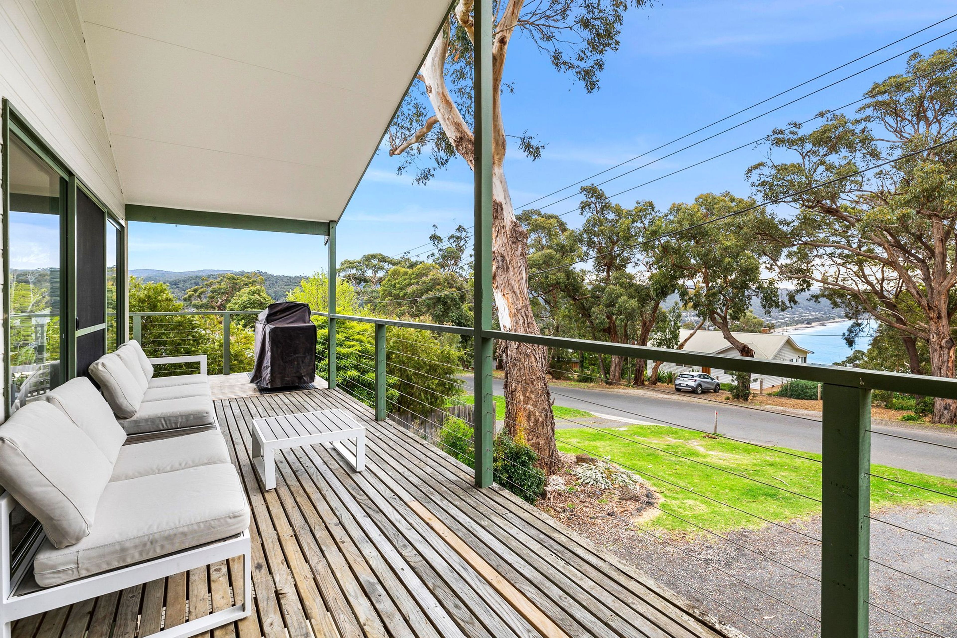 A balcony with a sofa and a grill, overlooking a road and greenery.
