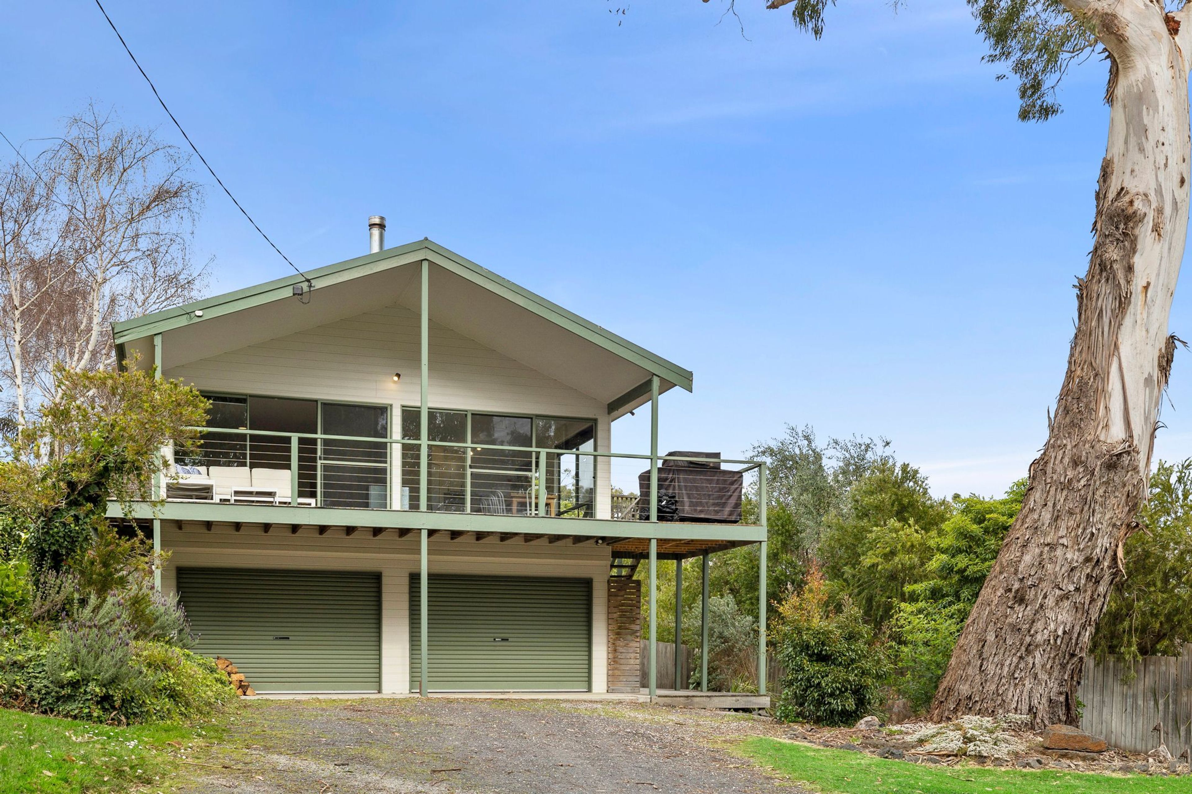 Ein zweistöckiges Gebäude mit Balkon, Garage und einem großen Baum im Hintergrund.
