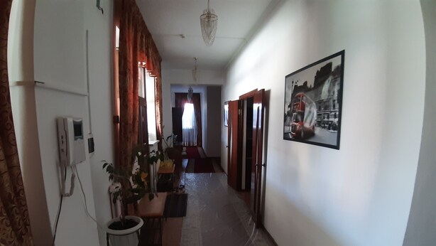 A narrow hallway with a dining area on the left, a red carpet leading to a door, and a framed picture on the right wall.