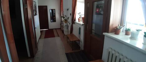 A narrow hallway with a radiator, a table, and a bench. There are potted plants on a windowsill.