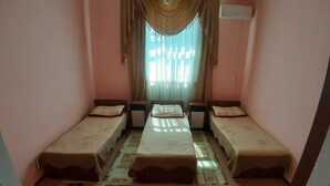 A room with three single beds aligned in a row, a window with curtains, and a patterned carpet.
