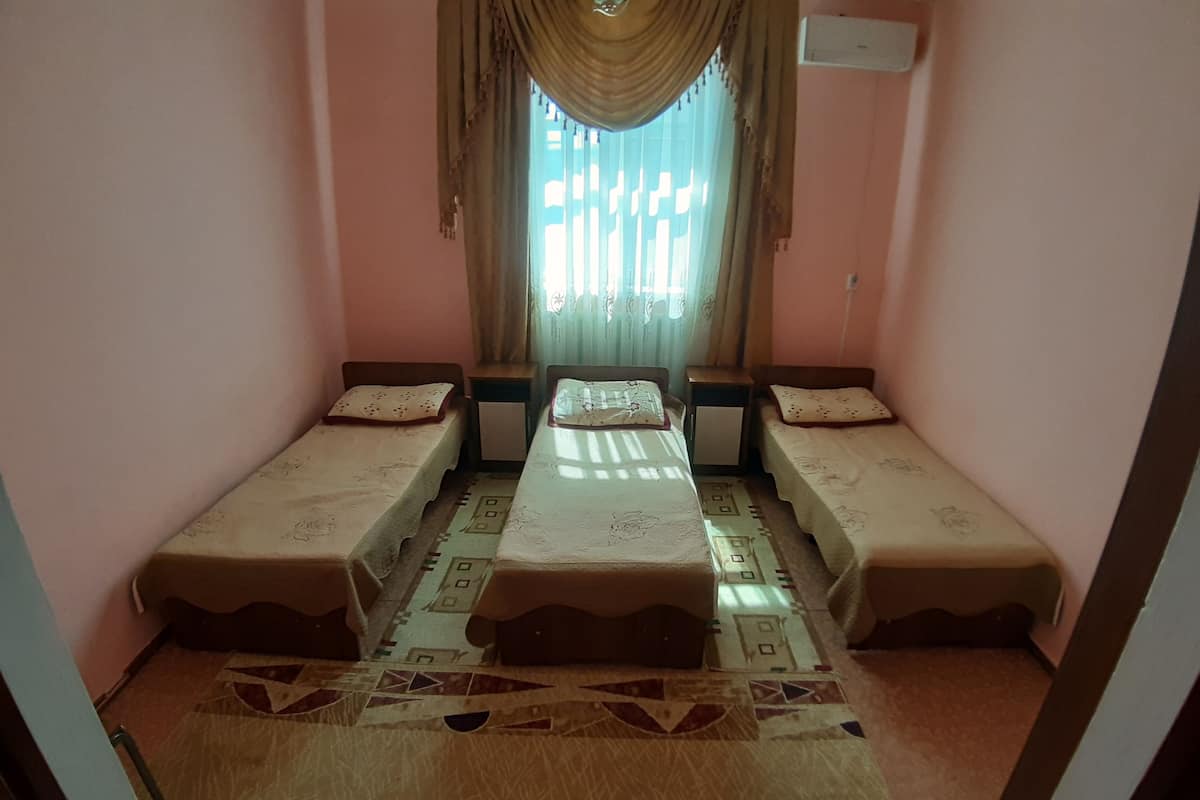 Une chambre avec trois lits simples alignés en rangée, une fenêtre avec des rideaux et un tapis à motifs.