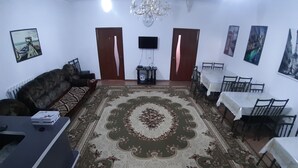 A living room with a large floral carpet, a sofa, a TV, and a dining area with chairs and a table.