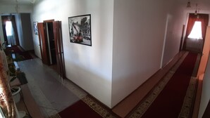 A hallway with a red carpet, a framed picture on the wall, and a door leading to another room.