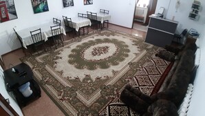A living room with a large patterned rug, a sofa, a dining area with tables and chairs, and a small black cabinet.