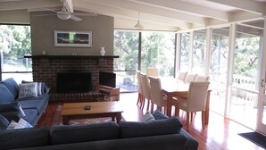 A living room with a fireplace, a sofa, a dining table with chairs, and large windows.
