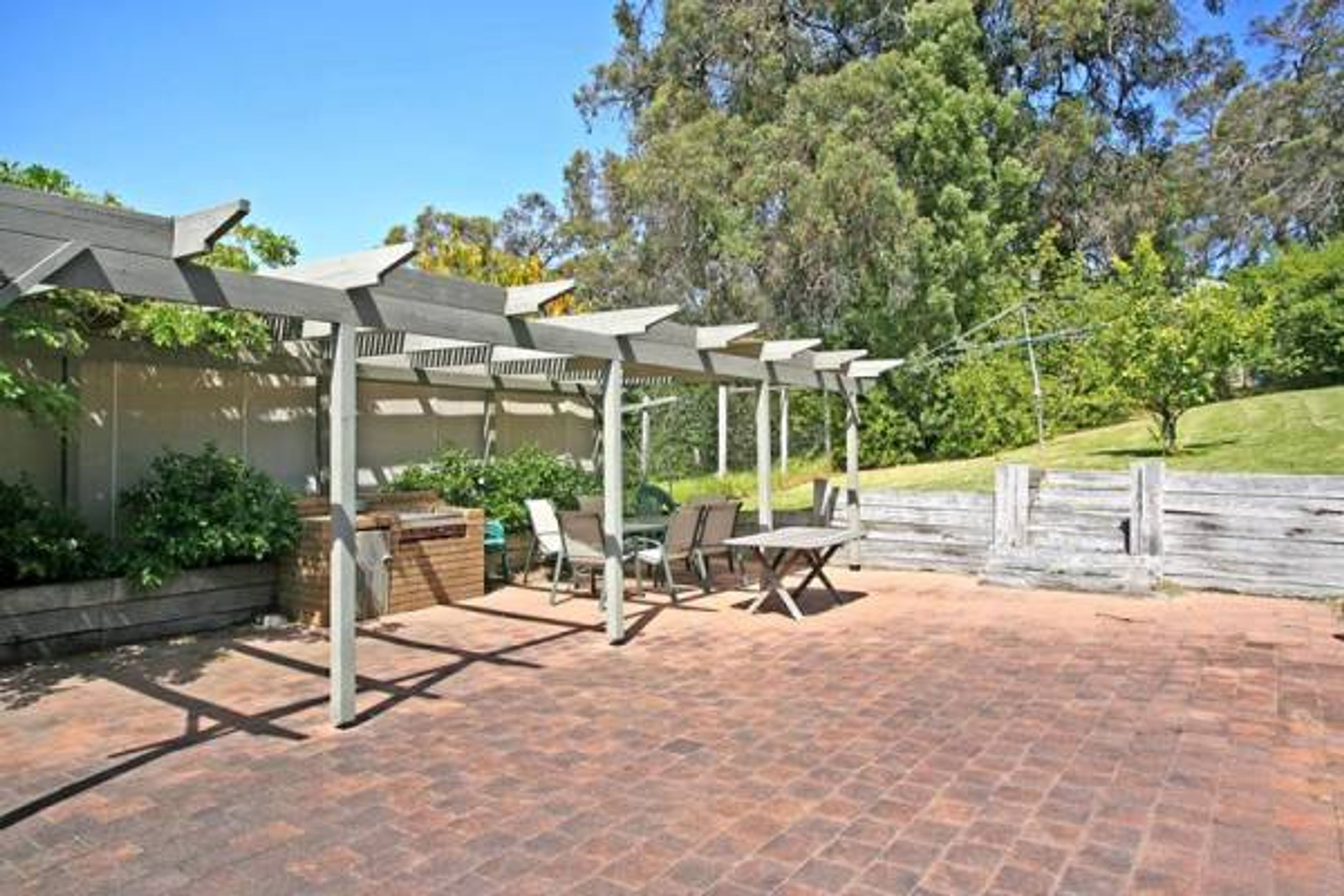 Une terrasse extérieure dotée d’une pergola, d’un espace salon et d’un sol en briques.