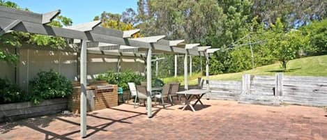 Une terrasse extérieure dotée d’une pergola, d’un espace salon et d’un sol en briques.