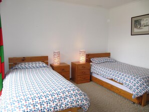 Een slaapkamer met twee eenpersoonsbedden, houten hoofdborden en nachtkastjes met lampen.