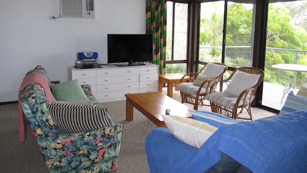 A living room with a television, sofa, chairs, and a view of greenery outside.