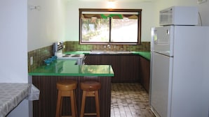 A compact kitchen with a green countertop, a white refrigerator, and a window with a view of greenery.