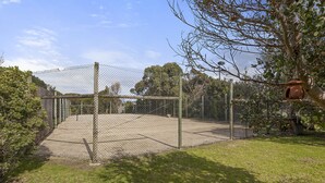 A fenced outdoor area with a concrete surface, surrounded by grass and trees. - Coastal Haven (Anglesea)
