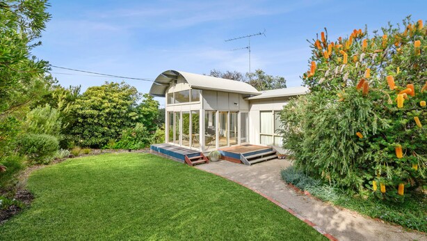 A modern house with a glass-enclosed porch, a well-maintained lawn, and a variety of shrubs and trees. - Coastal Haven (Anglesea)