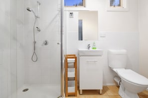 Un bagno con doccia, WC, lavandino e un piccolo sgabello di legno.