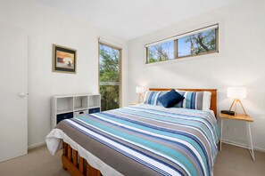 Ein Schlafzimmer mit einem Bett, Nachttischlampen, einem Beistelltisch, einem Fenster und einem gerahmten Bild an der Wand.