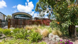 A landscaped garden with various plants and a building with a curved roof in the background. - The Pavillion (Lorne)