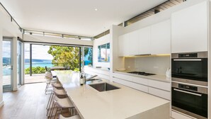 A modern kitchen with a large island, stainless steel appliances, and a view of the sea. - The Pavillion (Lorne)