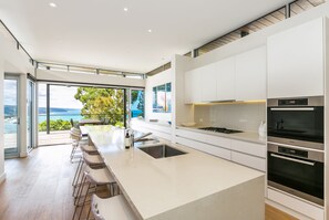 A modern kitchen with a large island, stainless steel appliances, and a view of the sea. - The Pavillion (Lorne)