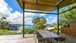 A spacious deck with a wooden table and chairs, overlooking a scenic view of a beach and ocean. - The Pavillion (Lorne)