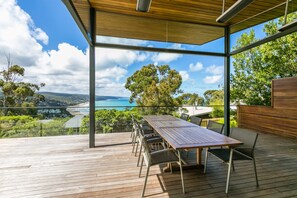 A spacious deck with a wooden table and chairs, overlooking a scenic view of a beach and ocean. - The Pavillion (Lorne)