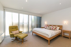 Une chambre à coucher avec un lit, une chaise, une table de chevet et une grande fenêtre.