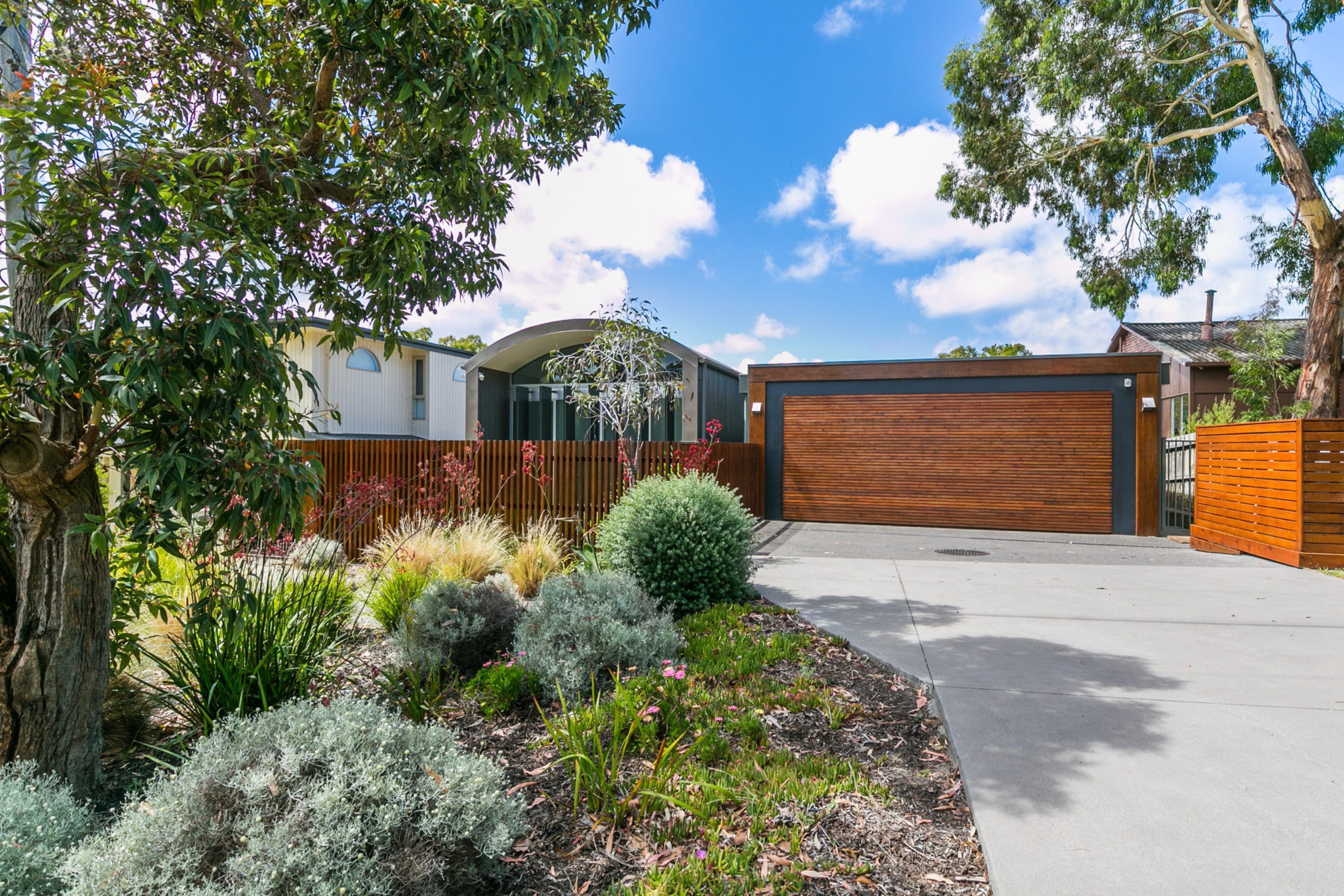 Une maison moderne dotée d’un grand garage, entourée d’un jardin aménagé avec différentes plantes et arbres.