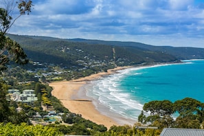 A coastal landscape with a beach, ocean, and forested hills. - The Pavillion (Lorne)