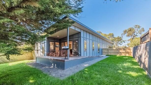 Une maison moderne dotée d’un patio couvert, d’un barbecue et d’une pelouse bien entretenue.