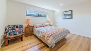 Une chambre à coucher avec un lit, une chaise, une table de chevet, une fenêtre et un tableau au mur.