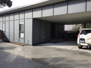 A modern building with a flat roof, large windows, and a covered parking area.