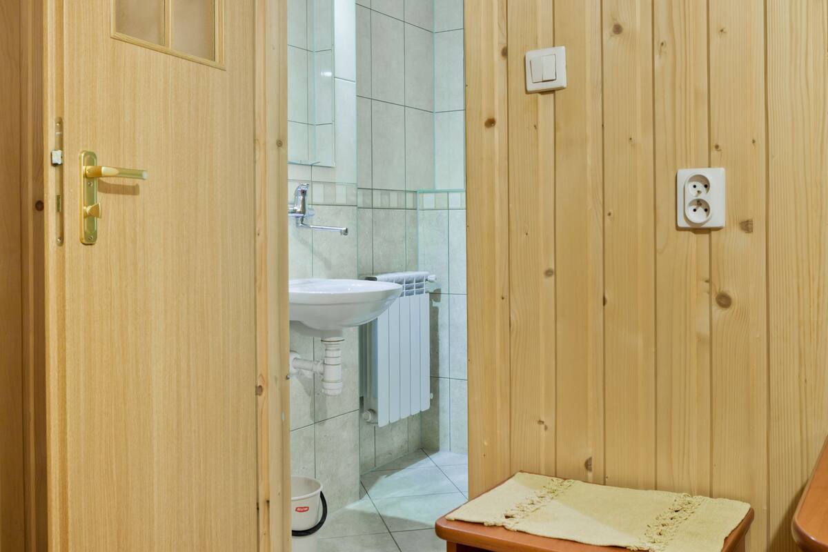 Un baño con paneles de madera, un lavamanos, un perchero para toallas y un pequeño taburete de madera.