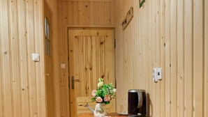Una habitación con paneles de madera, una mesa de madera, dos taburetes, un jarrón con flores y una cafetera.