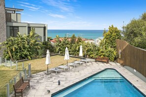 A pool area with a view of the ocean, surrounded by greenery and a wooden fence.