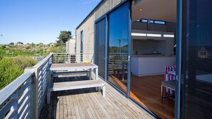 A modern house with a deck, a kitchen with a dining area, and a large sliding glass door. - Debonair 1 (Anglesea)