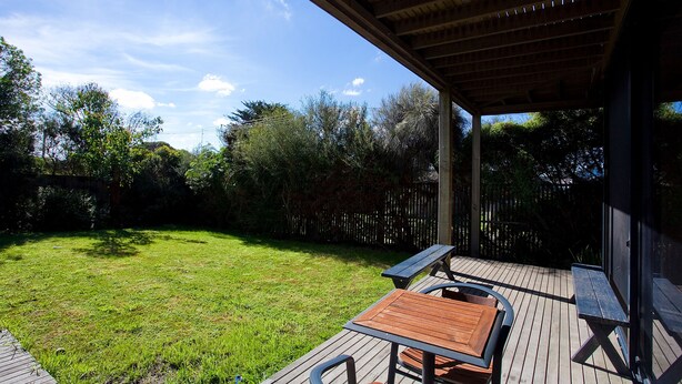 A wooden deck with a picnic table and chairs, surrounded by a grassy yard and a wooden fence. - Debonair 1 (Anglesea)