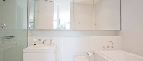Un bagno moderno con box doccia in vetro, lavabo con specchio sopra, water e vasca da bagno.