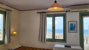 A room with a view of the sea, a bed, a table with a lamp, and a painting on the wall. - One Private Studio with stunning full sea view, shared pool and Ac (Heraklion Prefecture)