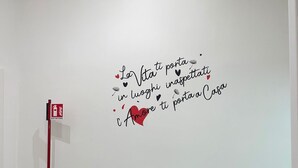 A bathroom with a grey cabinet, a small sink, and a fire extinguisher. A decorative wall decal with Italian text is visible. - Sleeping in Naples Center holiday house holiday home (Napoli)