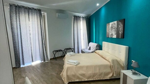 A modern bedroom with a large bed, a bedside table, a chair, and a window with curtains. - Sleeping in Naples Center holiday house holiday home (Napoli)