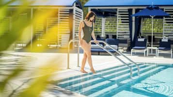 Eine Frau in Badebekleidung geht an einem Pool entlang, im Hintergrund liegen Liegestühle und Sonnenschirme.