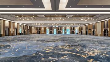 A spacious, well-lit conference room with a patterned carpet, modern chandeliers, and large windows.