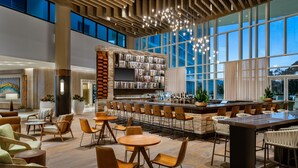 A spacious bar area with a long counter, multiple seating options including round tables and bar stools, and a large window providing a view of the outside. - JW Marriott Orlando Bonnet Creek Resort & Spa (Orlando)