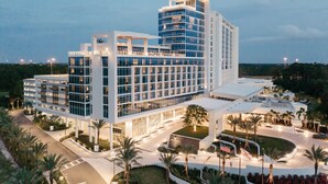 Un hotel moderno con varios pisos, una terraza en la azotea y un patio ajardinado.