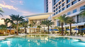 Un hotel moderno con piscina, palmeras y sombrillas azules.