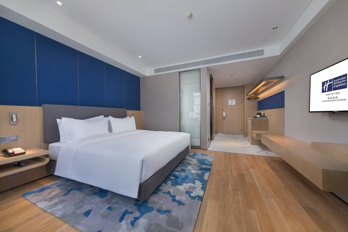 Une chambre d’hôtel moderne, dotée d’un grand lit, d’un bureau et d’un écran de télévision affichant le nom de l’hôtel.