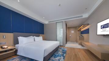 Een moderne hotelkamer met een groot bed, een bureau en een televisiescherm waarop de naam van het hotel staat.