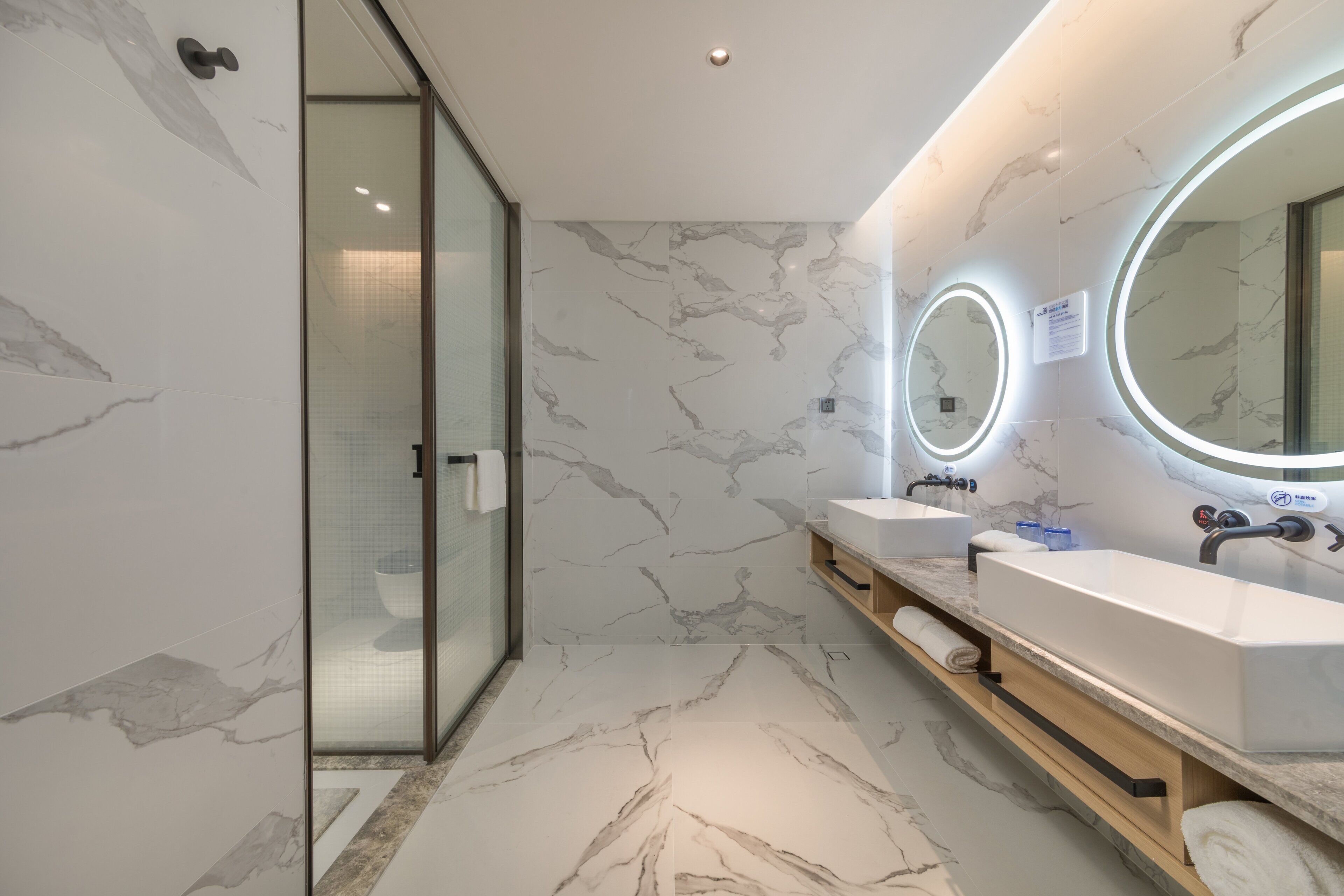 A modern bathroom with marble flooring, two sinks, and a glass shower enclosure.