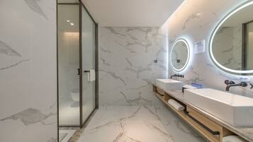 A modern bathroom with marble flooring, two sinks, and a glass shower enclosure.