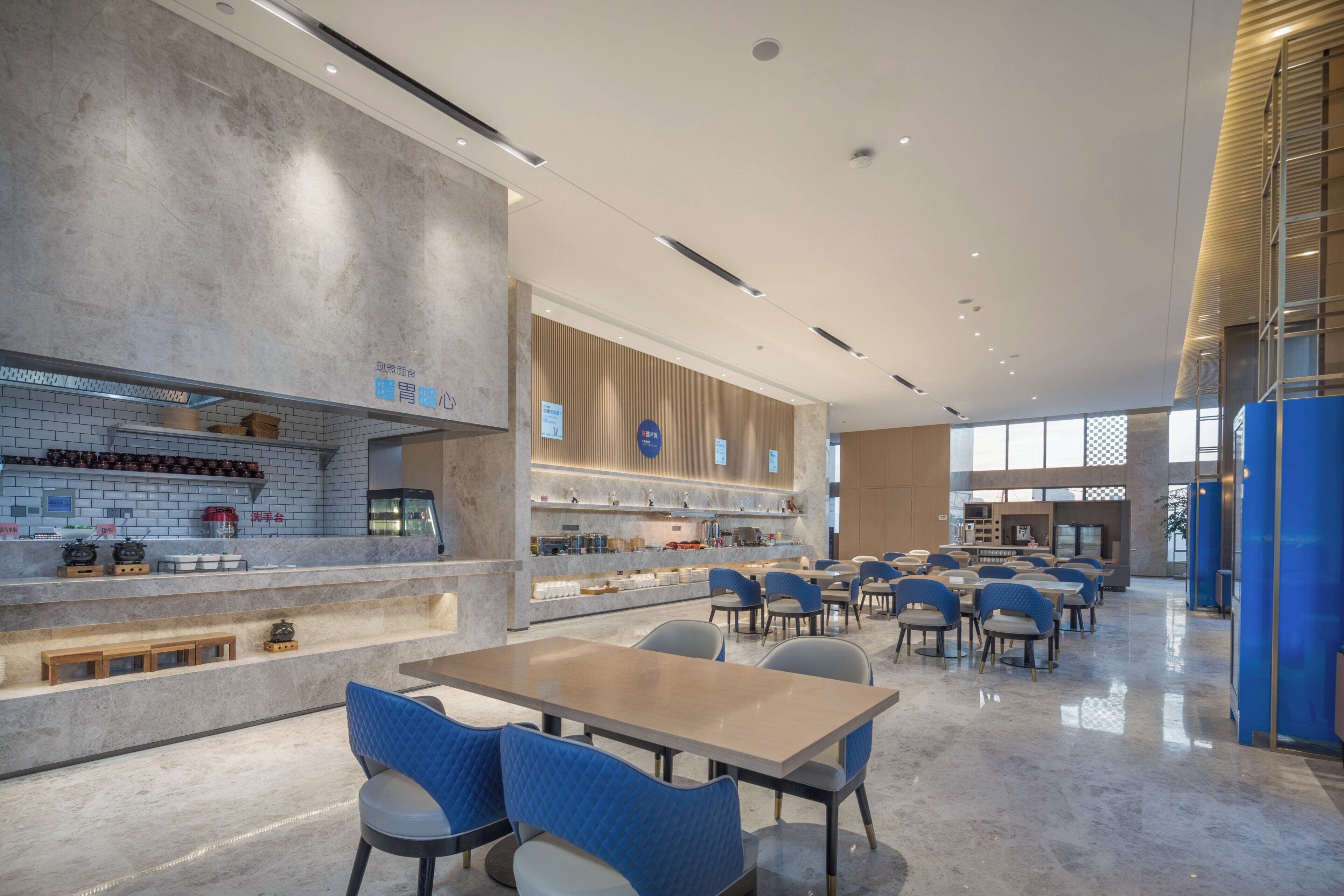 A modern dining area with a long counter, blue cushioned chairs, and a mix of marble and wood finishes.